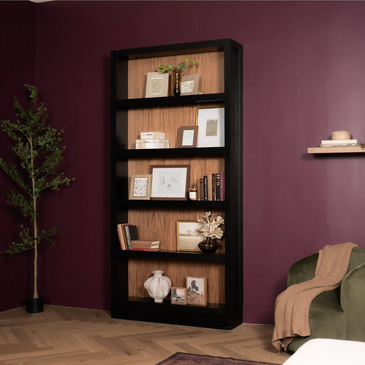 Murphy Door® hidden bookcase door. Tall black frame with wood-toned interior shelves, styled with decor in a red room.