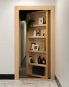 Murphy Door® light oak bookcase hidden door with decorative plants, framed art, and black vases on wooden shelves.
