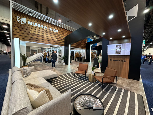 Murphy Door® exhibition booth at trade show featuring wood panel displays, modern seating area, and hidden door solutions.