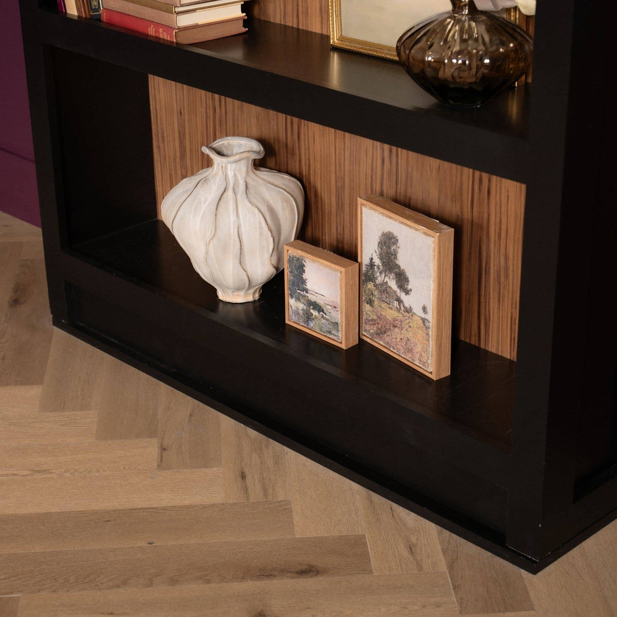 Dark Murphy Door® hidden bookcase holding books, a white vase, and framed art, with a wood back and herringbone floor.
