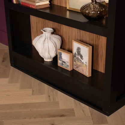Dark Murphy Door® hidden bookcase holding books, a white vase, and framed art, with a wood back and herringbone floor.