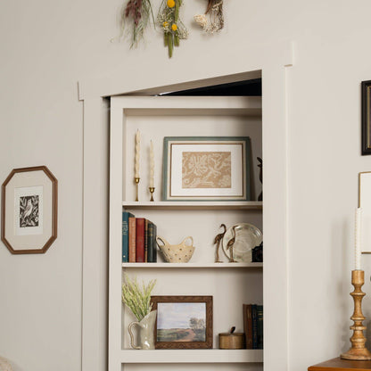 Murphy Door® DIY Quick Kit - Primed Only bookcase door, flush-mounted and filled with books and decor, seamlessly blends into a wall.
