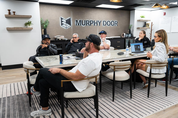 A business meeting at Murphy Door® headquarters with professionals gathered around a conference table beneath the company logo wall sign.