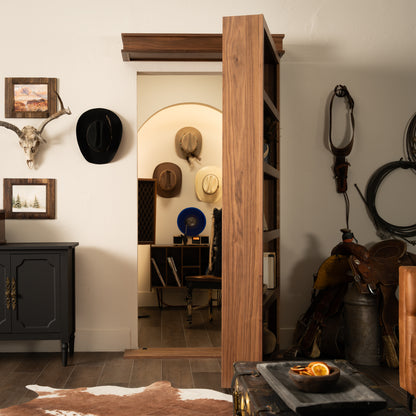 Murphy Door® wooden bookcase door with western decor, leading to room with cowboy hats on wall and rustic furniture.