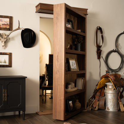 Murphy Door® wooden bookcase hidden door with western decor, featuring rustic shelving and cowboy-themed items in a southwestern style home.