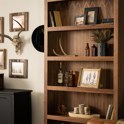 Stylish wooden Murphy Door® bookshelf with rustic western decor, antler display, and whiskey bottles on warm walnut shelving.