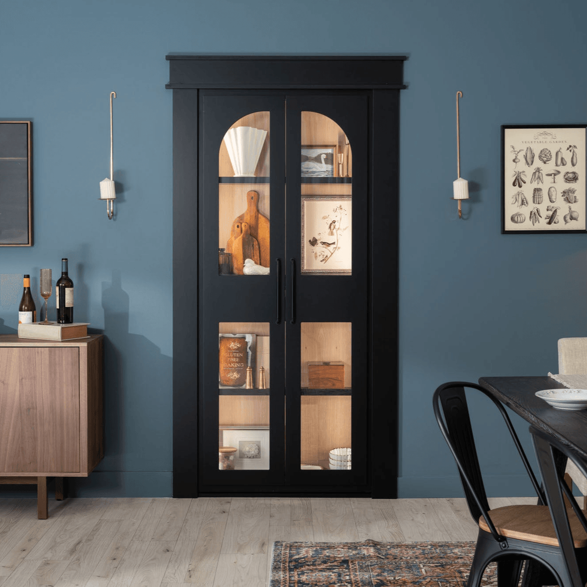 Murphy Door® black display cabinet with glass panels against blue wall, showcasing wooden cutting boards and decorative items.