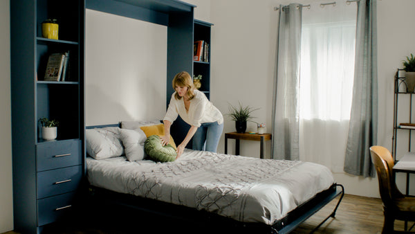 Murphy Door® wall bed system with navy cabinetry, white bedding, and decorative pillows in a modern, bright bedroom.