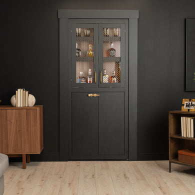 Murphy Door® dark gray liquor cabinet with mesh glass doors, brass handles, against black wall with wooden accents.