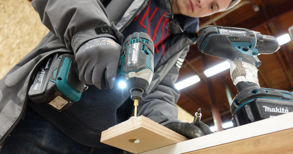 Person using Makita power drill to assemble wooden Murphy Door® component while wearing work gloves and jacket.
