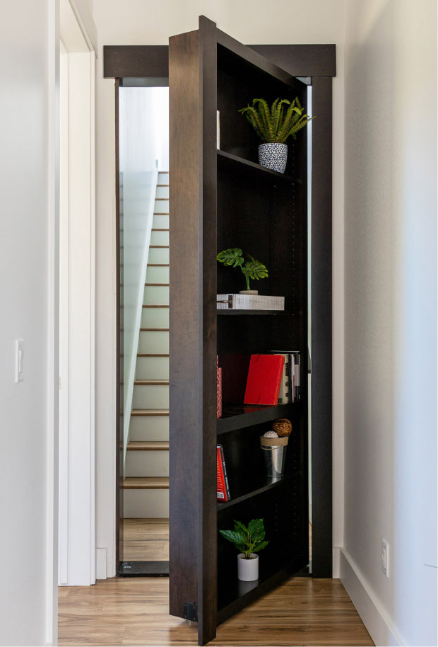 Murphy Door® bookcase hidden door in dark wood finish with shelves displaying plants and books, revealing staircase entrance.