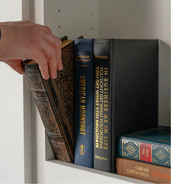 Hand selecting a book from Murphy Door® bookshelf; decorative hardcovers including "American Moonshot" arranged on white shelving.