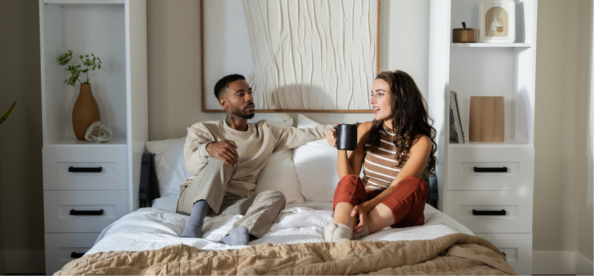 Two people relaxing on a Murphy Door® hidden bed, enjoying coffee in a minimalist bedroom with built-in storage and neutral decor.