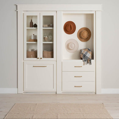 Murphy Door® white built-in cabinet with glass-front storage, drawers, and decorative niche displaying straw hats and plaid throw.