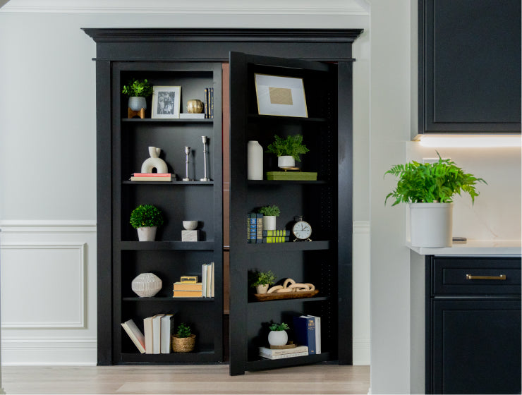 Murphy Door® black bookcase hidden door with one side open, showcasing stylish decor items and plants on multiple shelves.