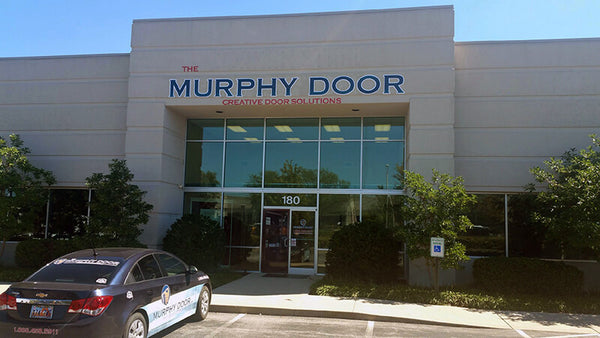 Murphy Door® storefront with large blue signage, glass entrance, company vehicle parked outside, building number 180 visible.