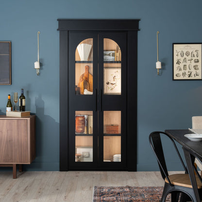 Murphy Door® black display cabinet with glass panels against blue wall, showcasing kitchen items and decor, with elegant lighting.
