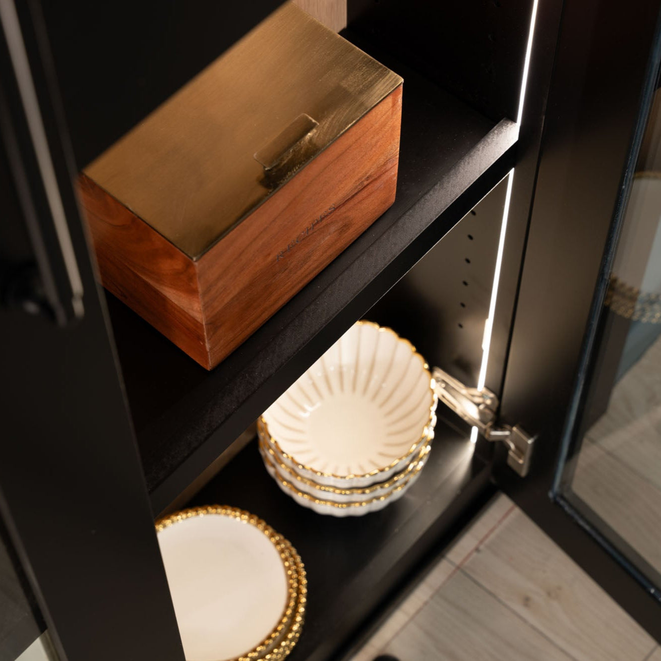 Murphy Door® black display cabinet with wooden box, gold-trimmed white decorative plates, and subtle LED lighting highlighting elegant storage solutions.