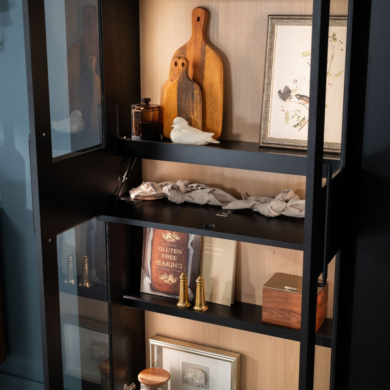 Murphy Door® black-framed cabinet with wooden cutting boards, gluten-free cookbook, and decorative items on light wood backing.