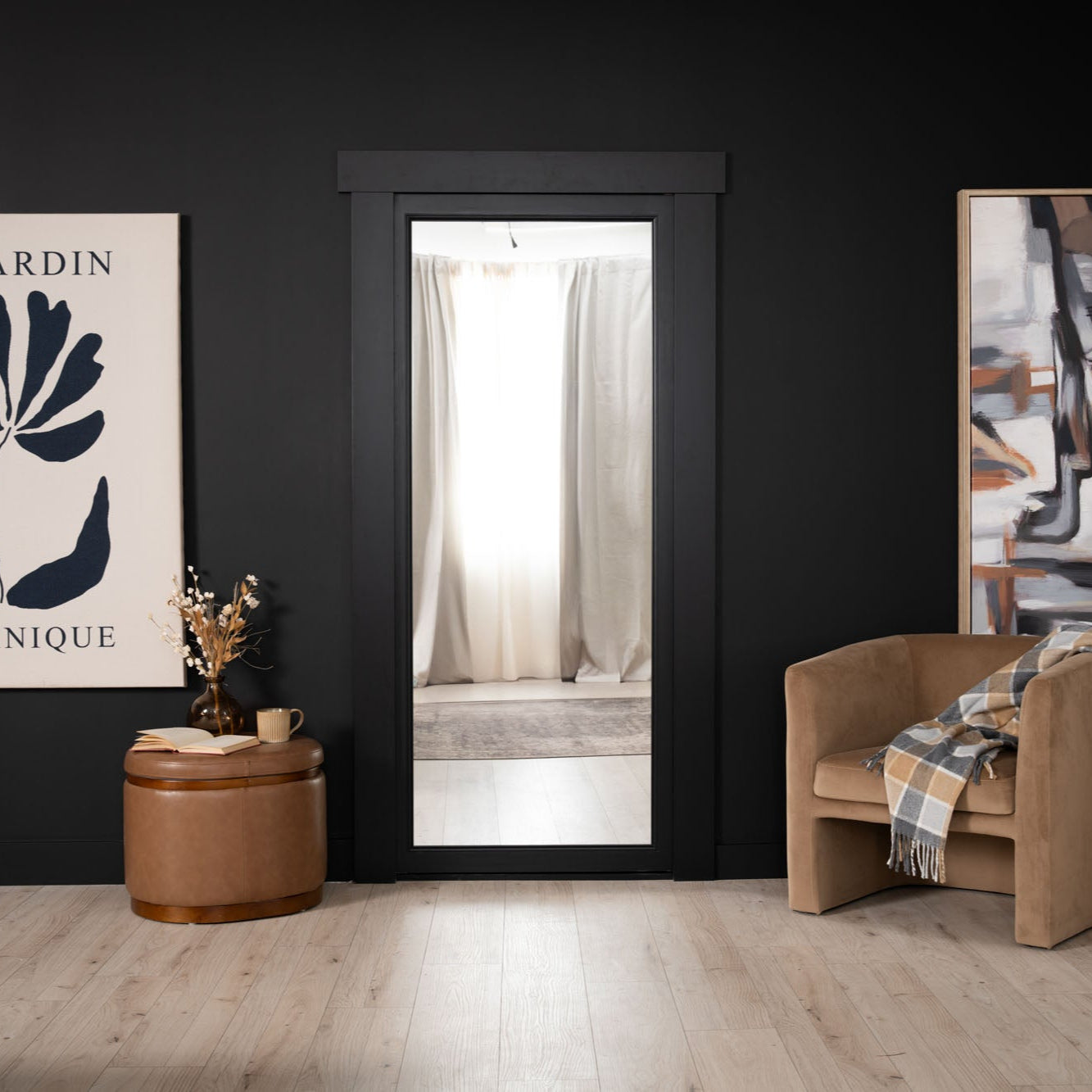 Murphy Door® black-framed doorway with light interior, camel accent chair, leather ottoman, and minimalist wall art in modern space.