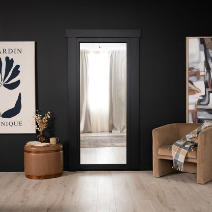 Murphy Door® black-framed doorway with light interior, camel accent chair, leather ottoman, and minimalist wall art in modern space.