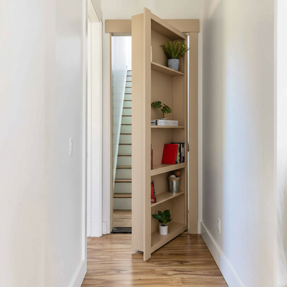 Paint Grade MDF / Unfinished finish variation for Murphy Door® bookcase hidden door in dark wood, partially open to reveal stairs, with decorative plants and books on shelves.