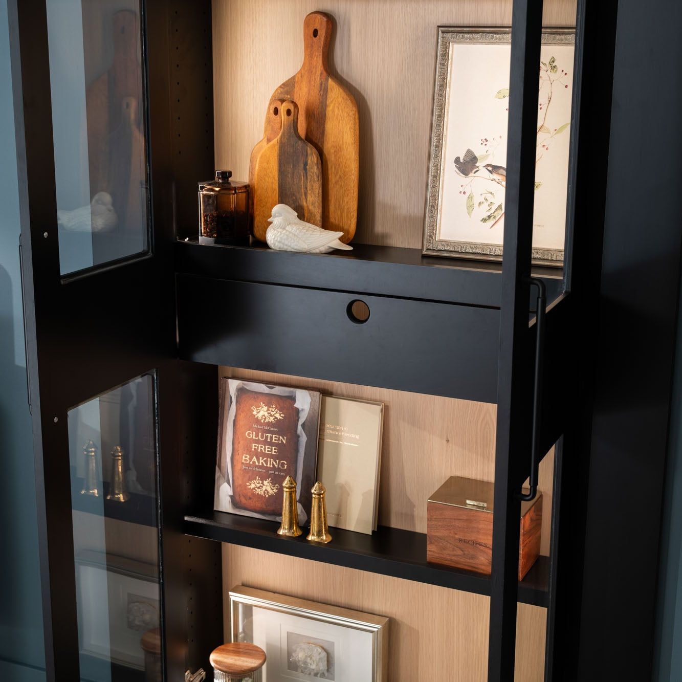 Murphy Door® bookshelf with wooden cutting boards, gluten-free cookbook, framed art, and decorative items in black and light wood finish.