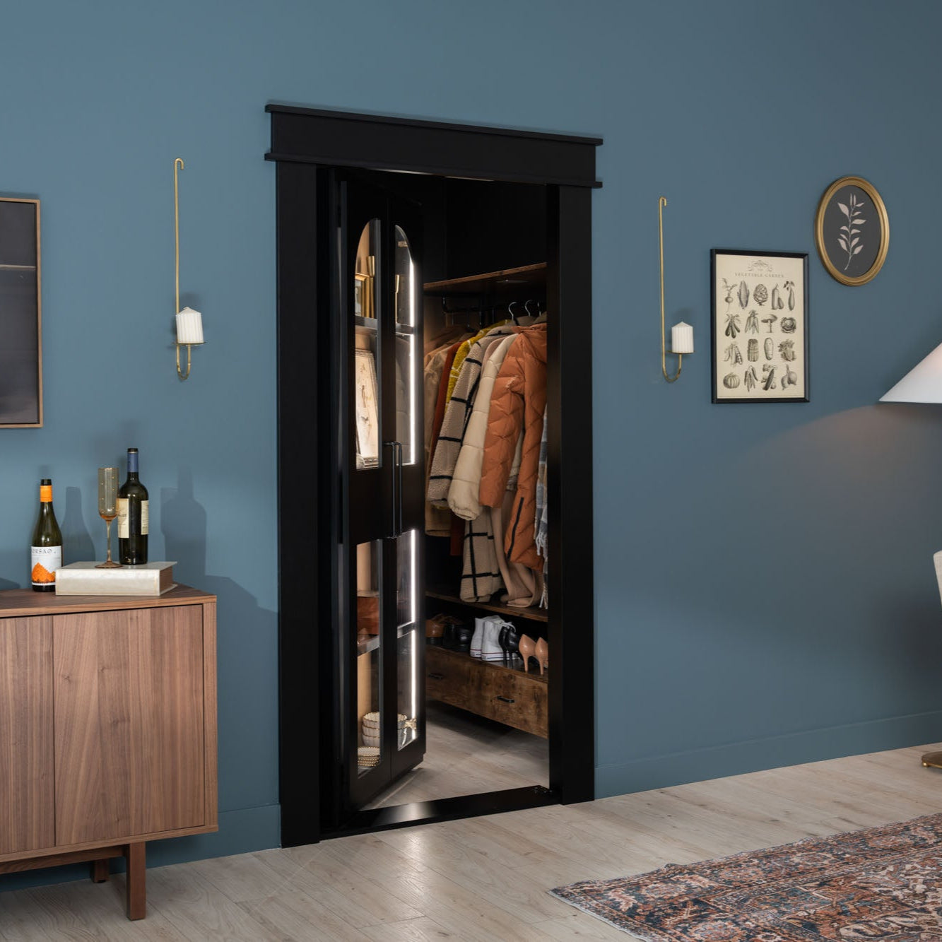 Murphy Door® hidden closet with sleek black glass door against blue walls, revealing organized winter coats and shoes inside.