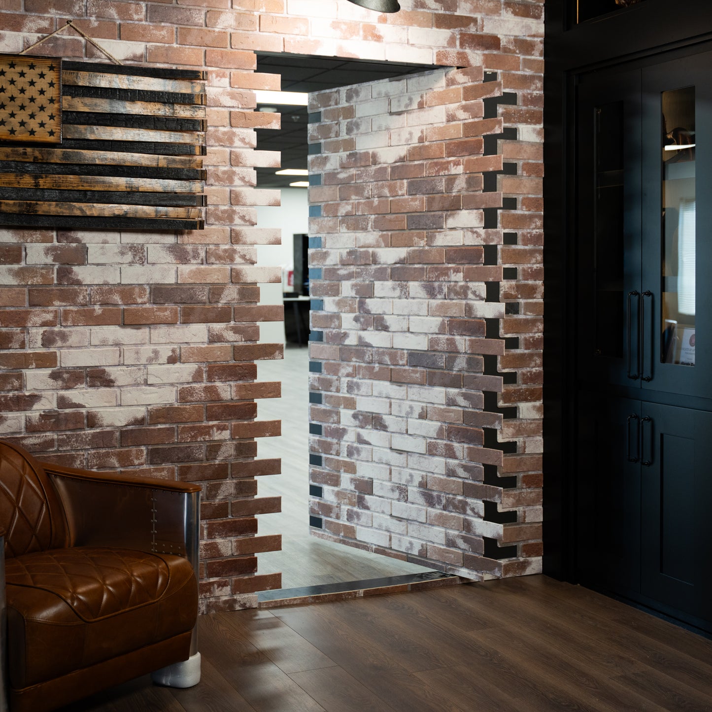 Murphy Door® hidden door, seamlessly integrated into a rustic brick wall, partially open, with a leather armchair.