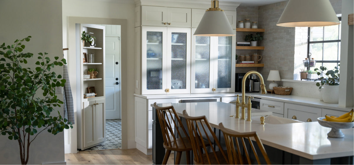 Elegant kitchen with white cabinetry, brass fixtures, wooden island seating, and a Murphy Door® entryway visible to the left.