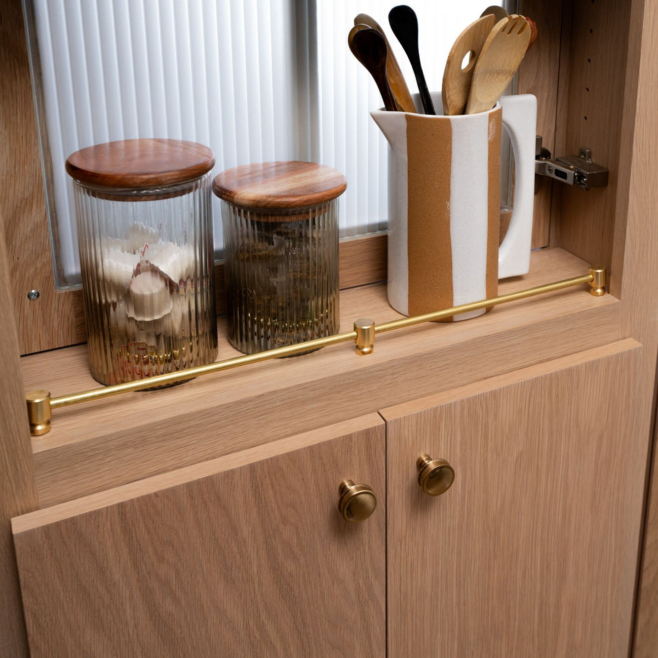 Murphy Door® kitchen cabinet with wooden glass storage jars, ceramic utensil holder and brass rail detail.