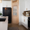 Murphy Door® light oak pantry door with glass panes in white kitchen featuring black refrigerator and geometric backsplash.