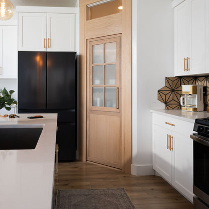 Murphy Door® light oak pantry door with glass panes in white kitchen featuring black refrigerator and geometric backsplash.