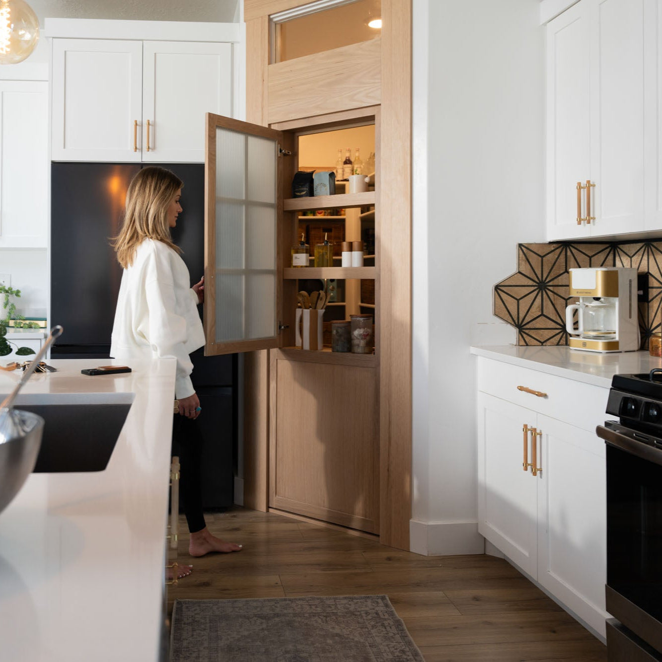 Murphy Door® pantry hidden door solution with light wood finish, integrated shelving, and sleek white kitchen with gold hardware.
