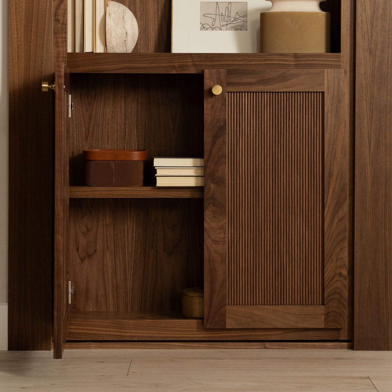 Murphy Door® walnut cabinet with ribbed sliding door panel, brass hardware, and interior shelving displaying decorative items.