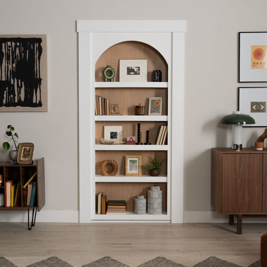 Murphy Door® white bookcase hidden door with arched top, wooden backing, and stylish decorative objects on five shelves.