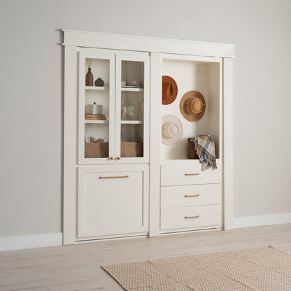 Murphy Door® white built-in storage cabinet with glass doors, drawers, and display niche featuring decorative hats and baskets in neutral tones.