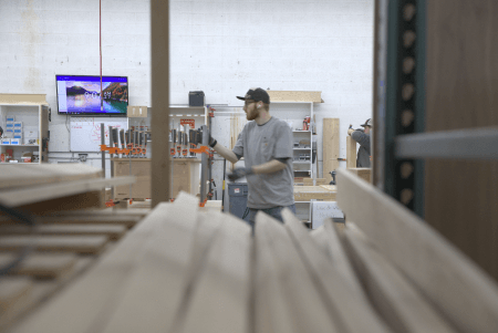 Woodworker in Murphy Door® manufacturing facility with lumber in foreground and TV displaying scenery in background.