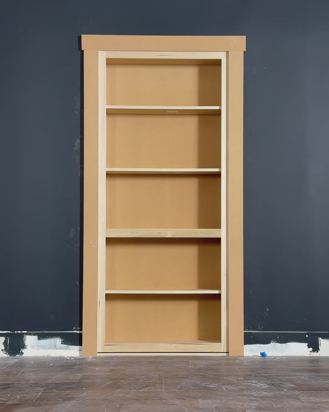 Man installs Murphy Door® Hidden Door Starter Kit (DIY bookcase door) into a dark gray wall, demonstrating its flush-mount swing.