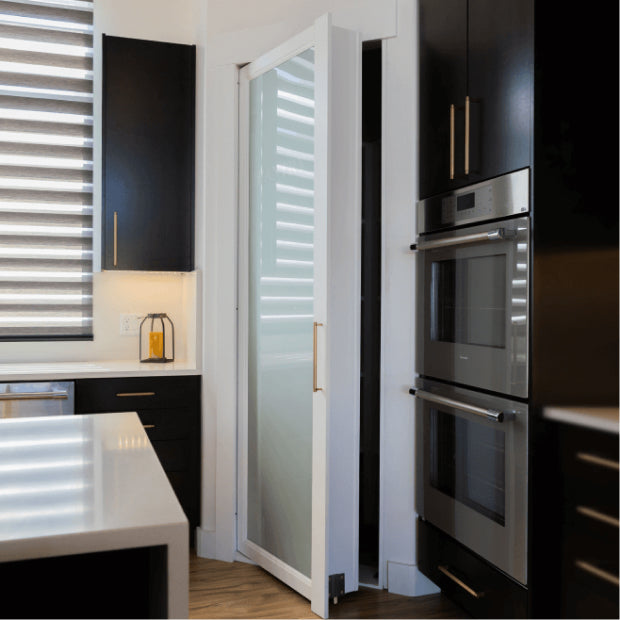 Murphy Door® white frosted glass pantry door with sleek gold handle in modern kitchen with black cabinets and stainless appliances.