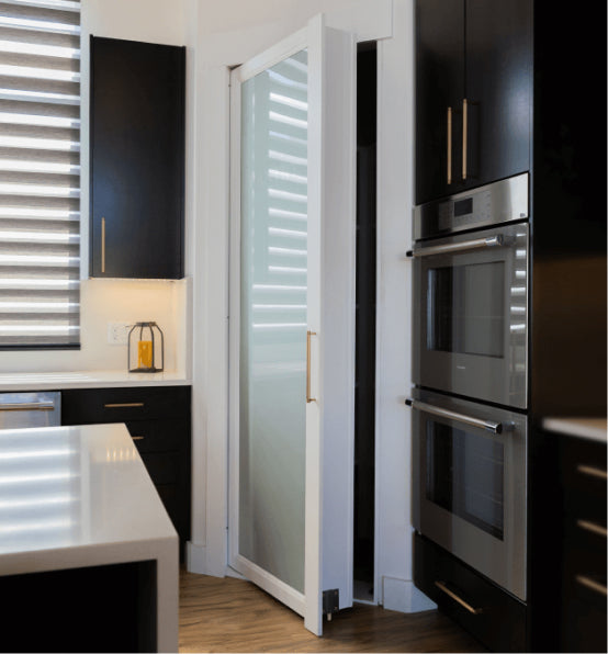 Murphy Door® frosted glass pantry door with sleek handle, set in modern kitchen with black cabinets and stainless steel ovens.