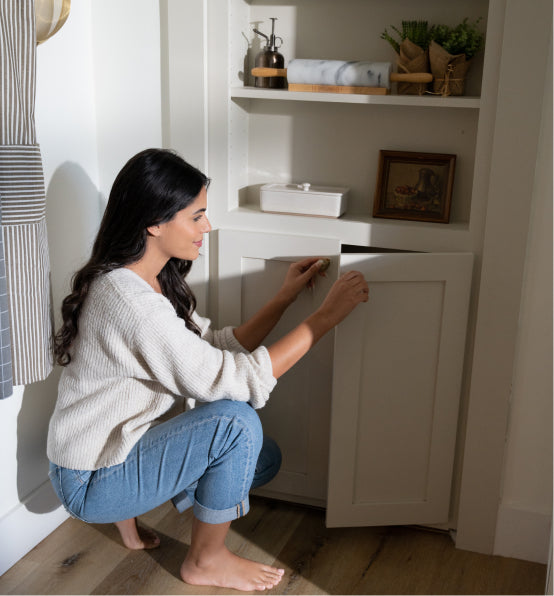 Person opening a Murphy Door® hidden cabinet in white built-in shelving unit, wearing light sweater and blue jeans.